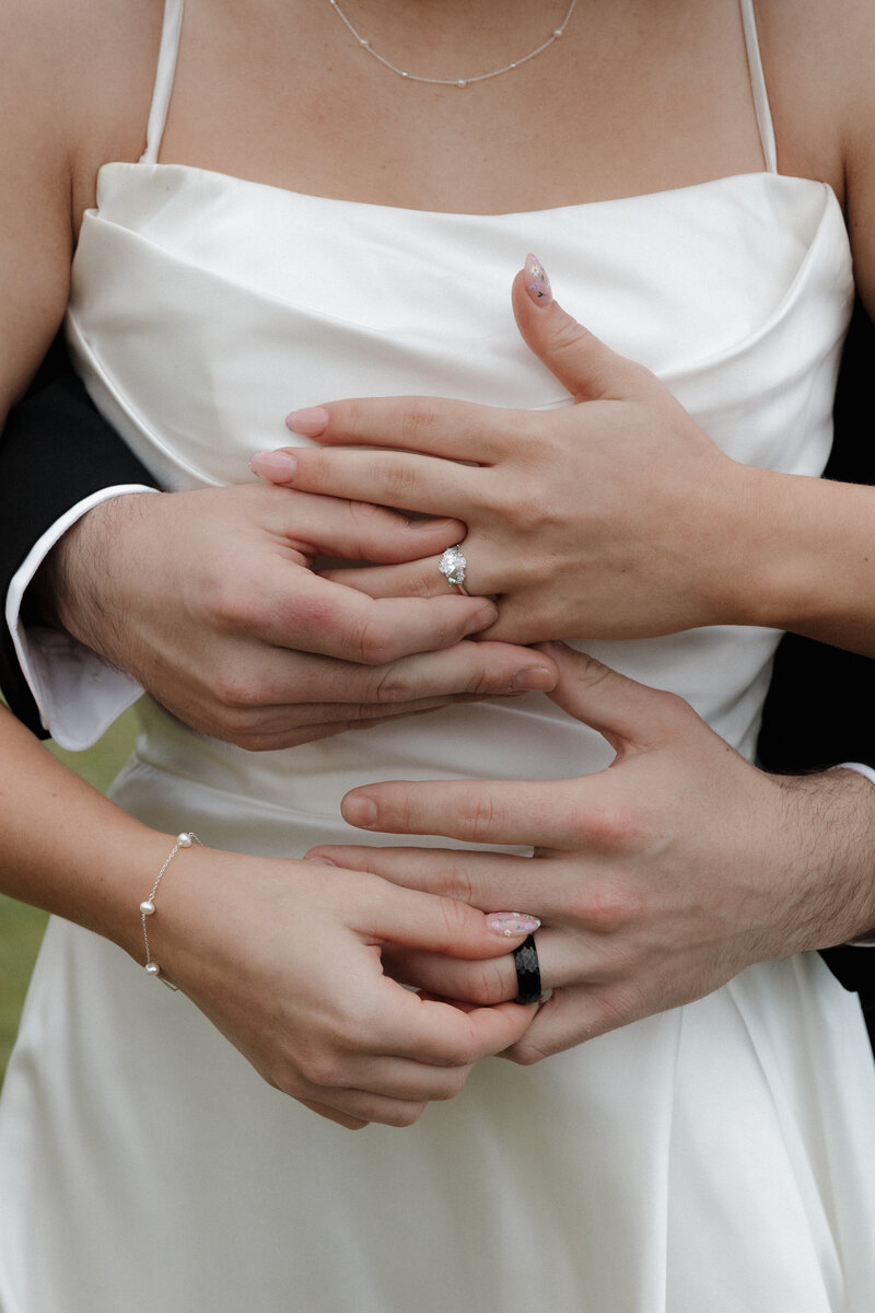 Wedding ring shot with bride and grooms hands in front of wedding dress
