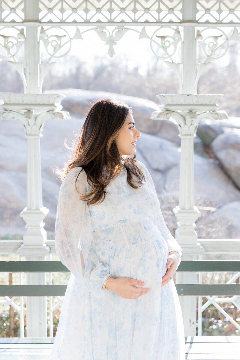 Woman in blue floral dress holding pregnant belly