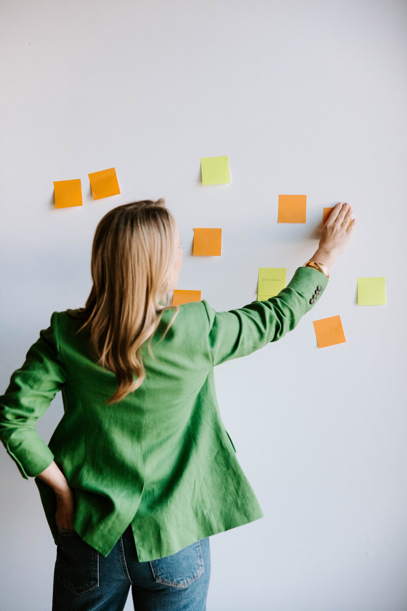 Heather Frick executive coach in a green blazer putting orange and yellow sticky notes on a wall