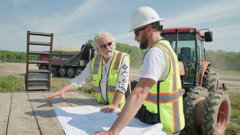 Marty and team looking at blueprints in front of tractor
