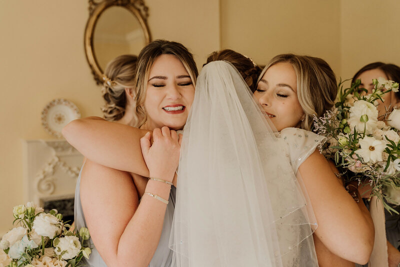 Bridesmaids giving bride with veil a hug