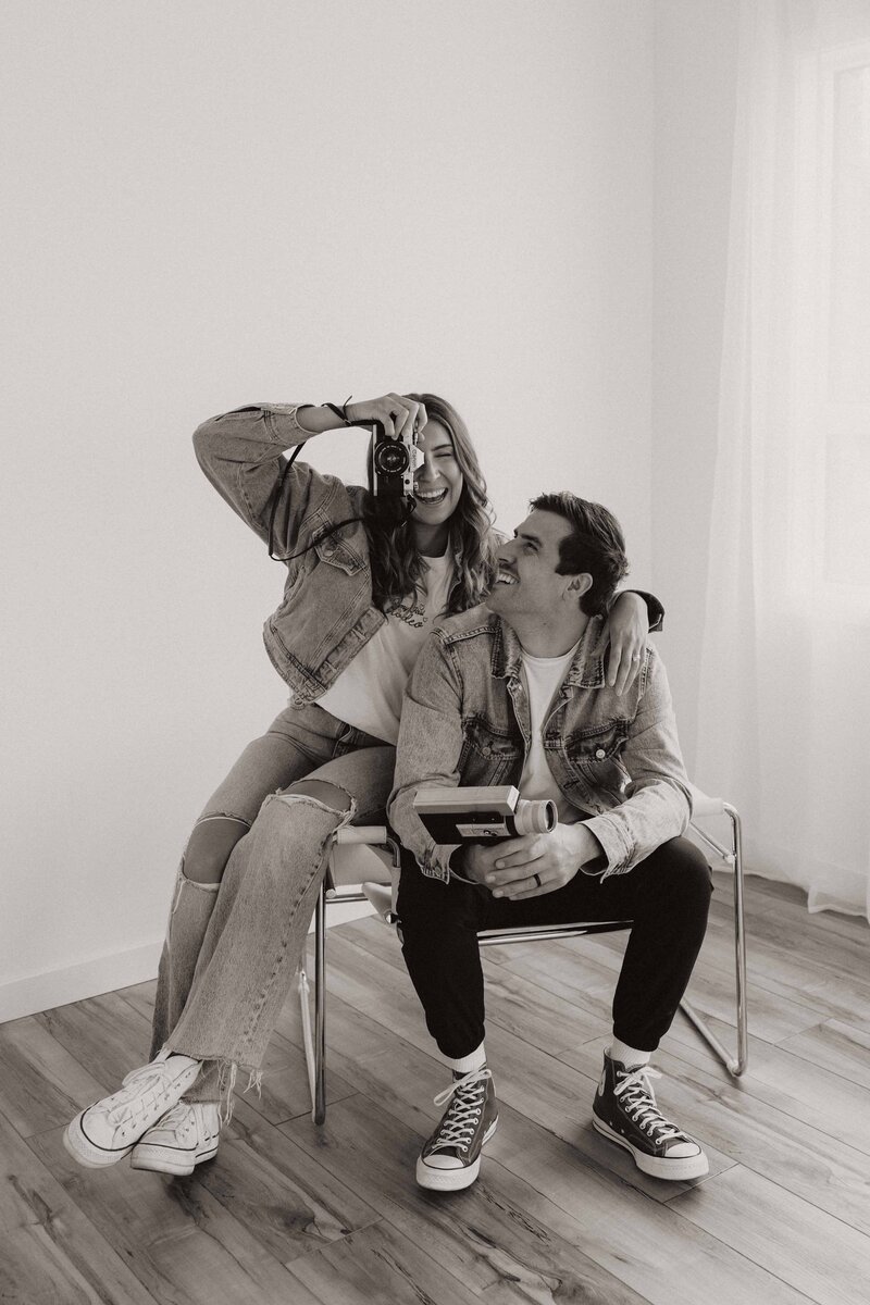 Hannah and Tyler sharing a chair, with Hannah holding a camera up to her eye as Tyler looks at her