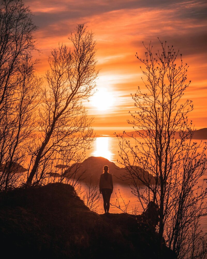 A woman standing by a lake looking at the sunset.
