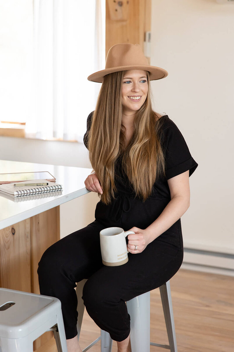 Laurel of Laurel Deane Creative smiling and sitting at a counter while holding a coffee cup