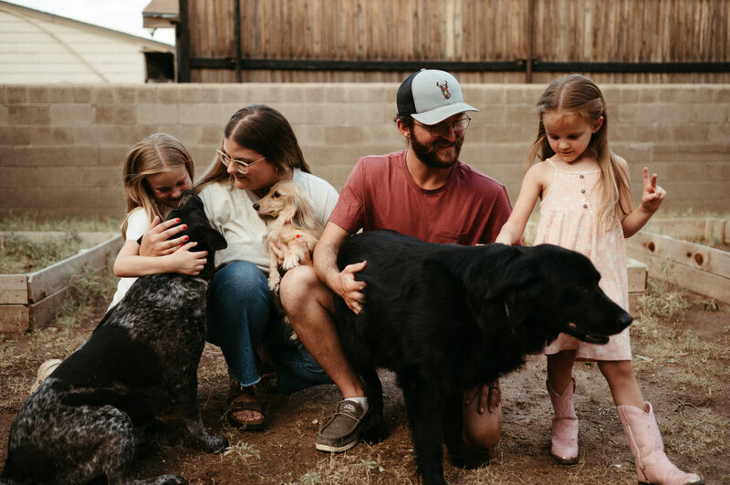 Family of four loving on their pups in the backyard.