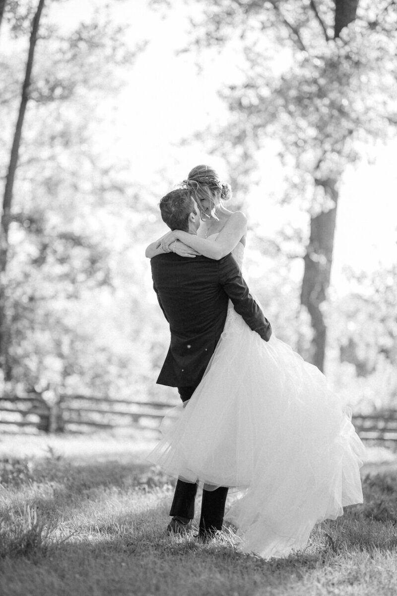 The groom lifts his bride in a joyful spin by the water in Montérégie — a tender and romantic scene captured during a naturally charming wedding in Quebec