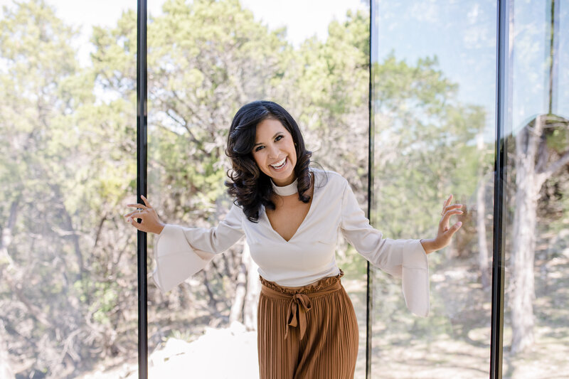 woman in a cream shirt and brown pants leans into a room while standing in a glass doorway photographed by Orlando photographer