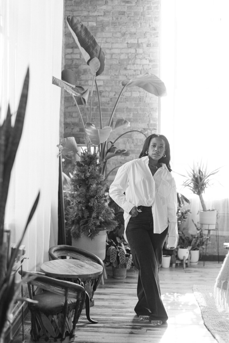 Chicago certified sex therapist standing in a plant filled brick room in a white tshirt and jeans
