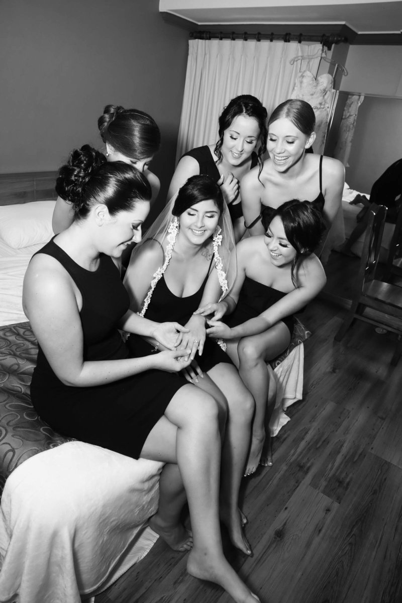 B+W image of bride showing off her engagement ring to her bridesmaids while they get ready for the big event. Photo by Ross Photography, Trinidad, W.I..