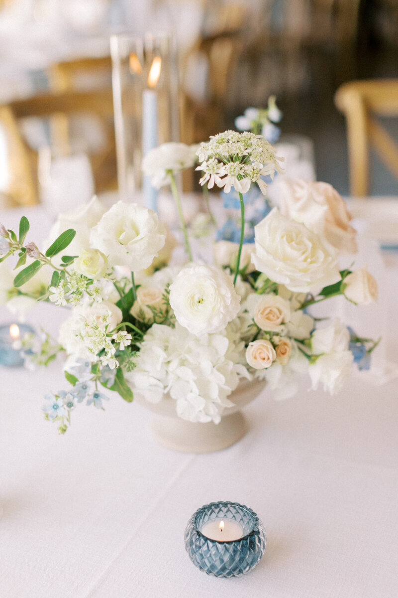 A close up of a floral arrangement with primarily white flowers and a candle burning in the background.
