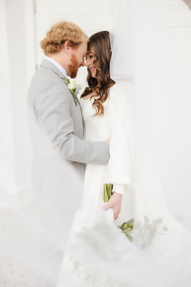 A bride and groom standing forehead to forehead while smiling at each other. 