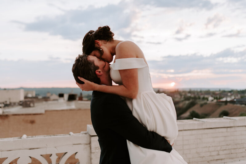 A bride and groom holding hands while walking together on  a rooftop during sunset.