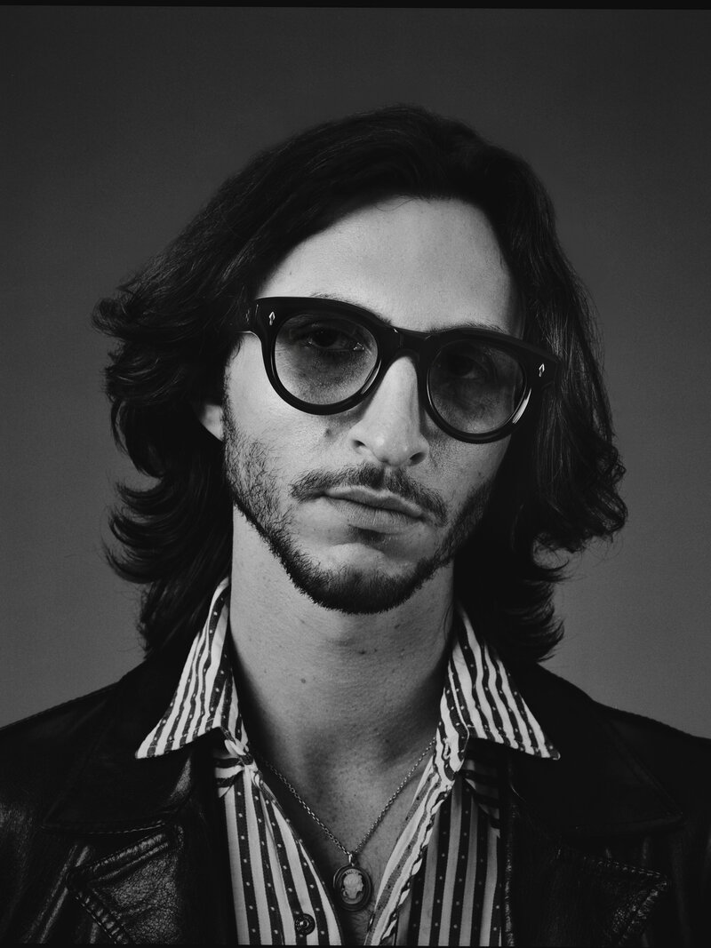 A man wearing thick rimmed Dita glasses with a white shirt and black hair.