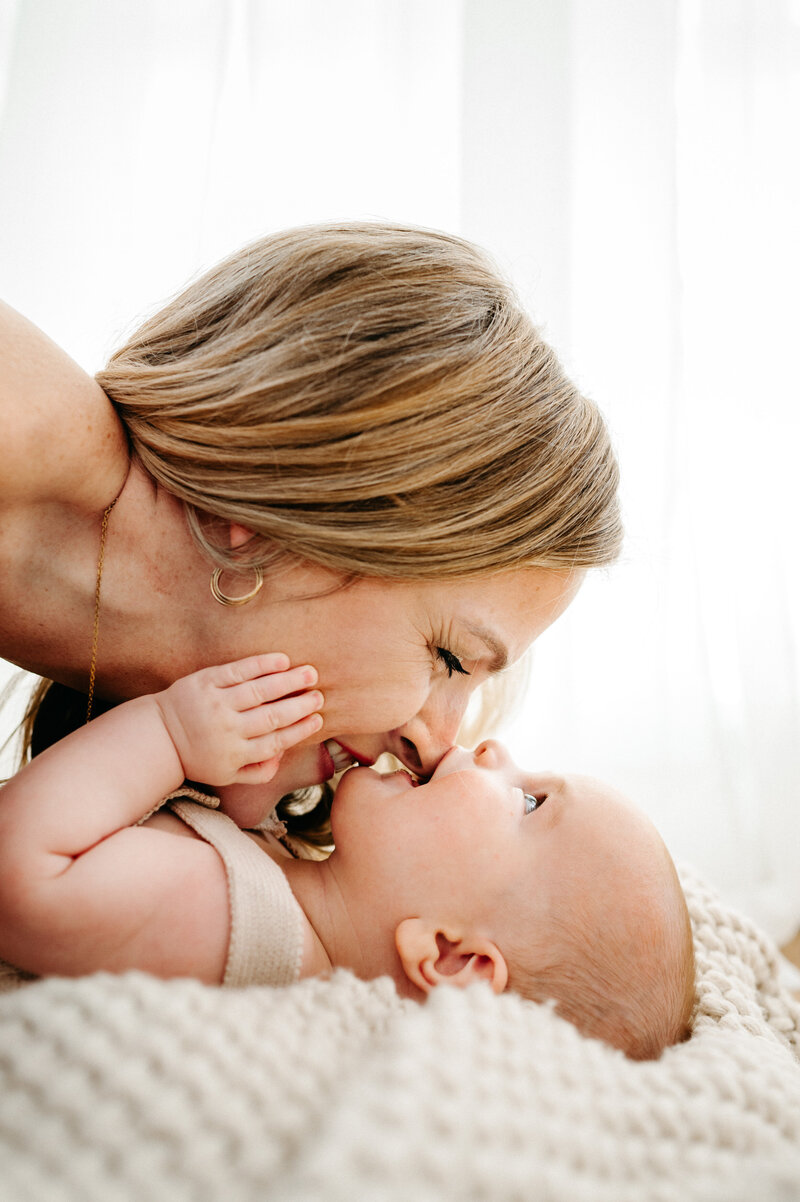 A mother leaning over her baby to share a kiss. 