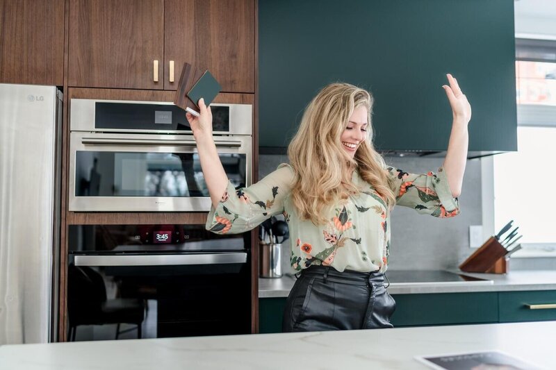 Okanagan interior designer in stylish outfit celebrating in a bright modern kitchen for business lifestyle photoshoot.