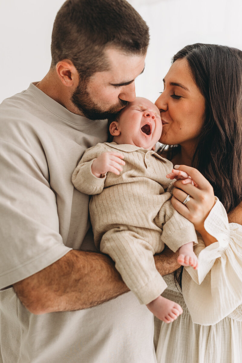 Newborn photos in kelowna b.c. with baby's parents giving baby a kiss and baby yawning