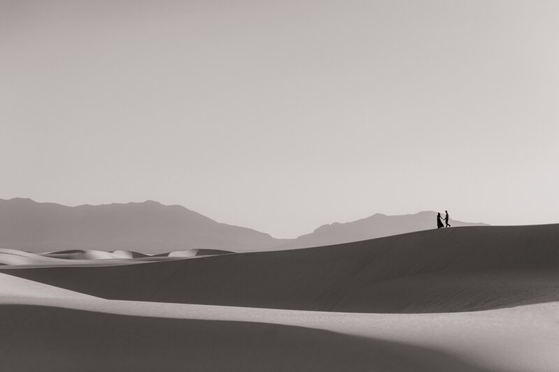 Couple walking on crest of sand dune in the distance during a destination wedding