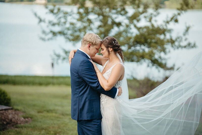 A newlywed couple with their arms around each other standing head to head 