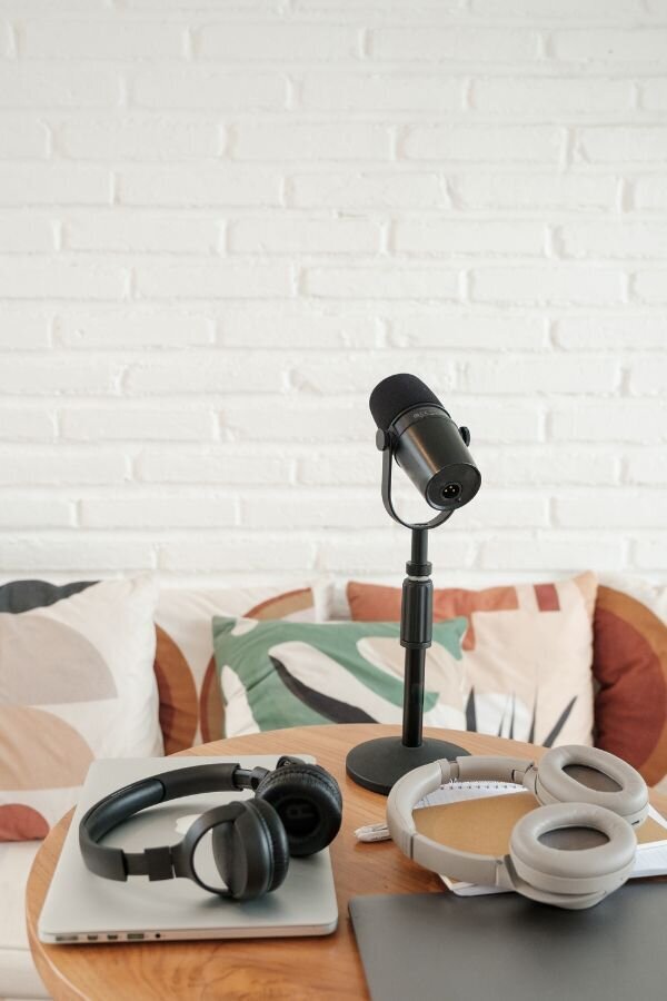 A laptop, headphones, and a microphone arranged neatly on a wooden table, suggesting a workspace for audio or video production.