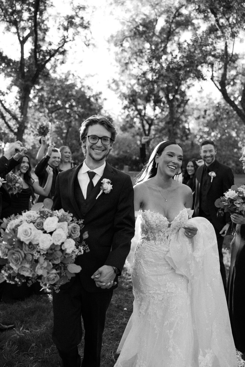 A bride and groom holding hands and smiling as they walk in between their guests.