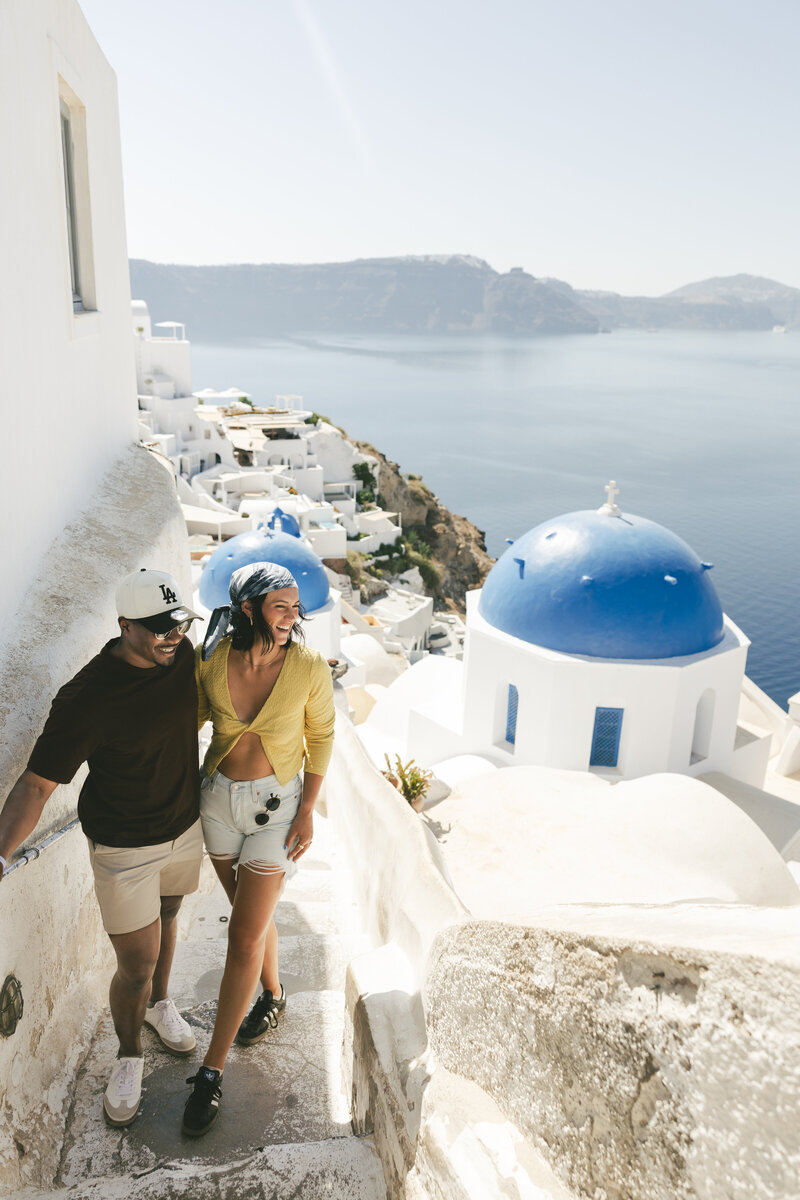 Georgia and Micah smiling by the blue-domed churches of Oia, Greece.