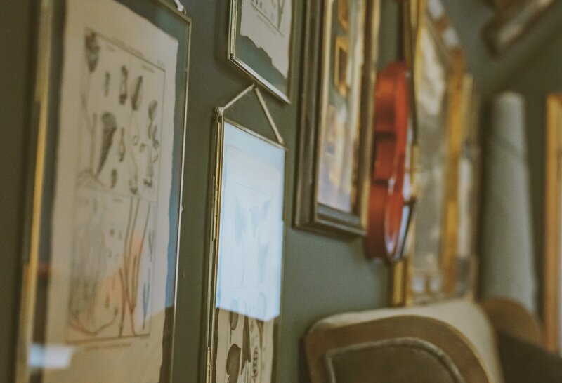 Gallery wall with antique plant prints, other artwork and violin along with a sofa bench and a roll of fabric in the corner