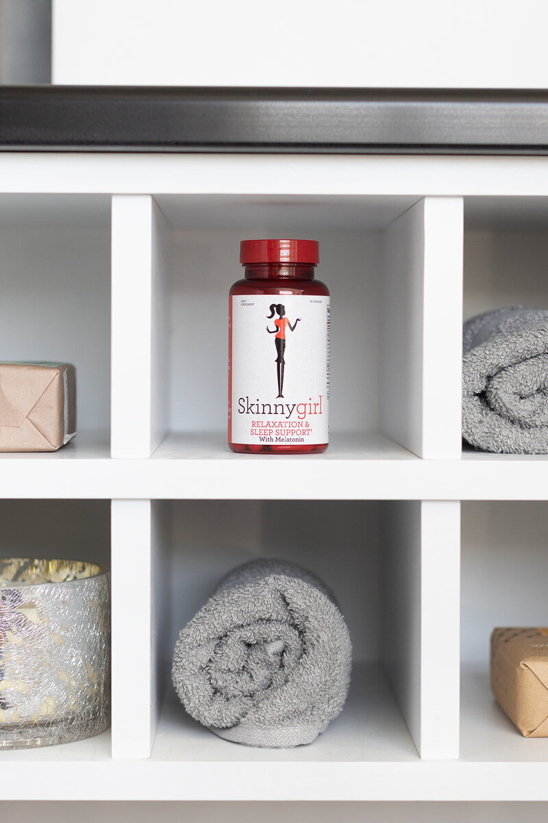 Skinnygirl Vitamins on a white shelf surrounded by towels