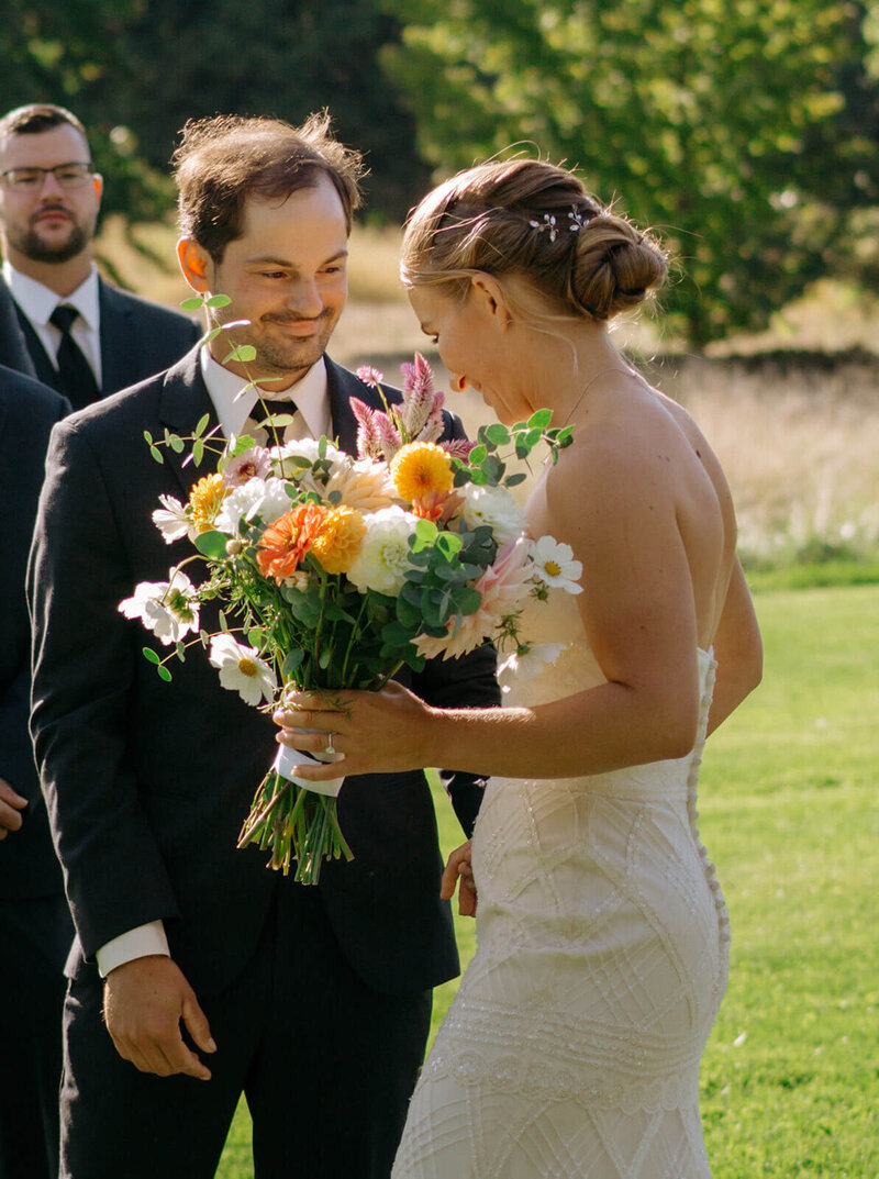 The groom is smiling while standing near the altar, seeing the bride.