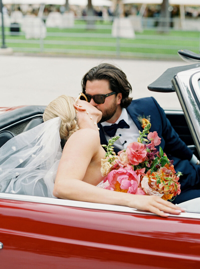 Close-up of Kelly’s bouquet with coral, peach, and blush peonies resting on the door of a red convertible post-ceremony, designed by Summer Robbins Flowers in Bend, Oregon