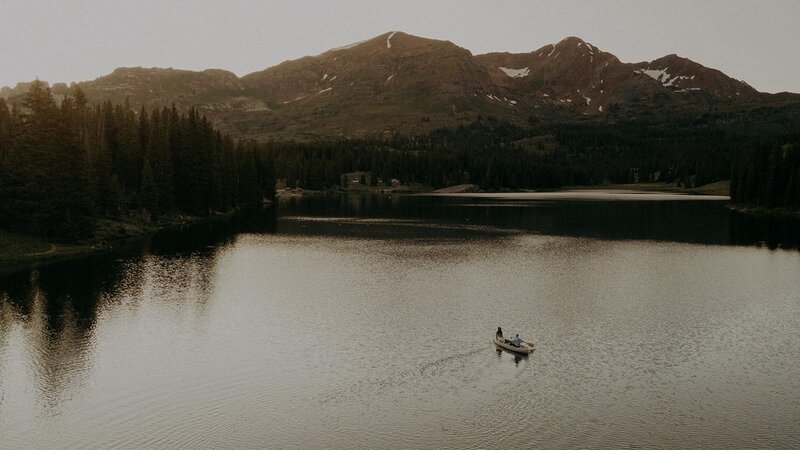 A drone image of two people in a canoe in a lake with mountains in the background