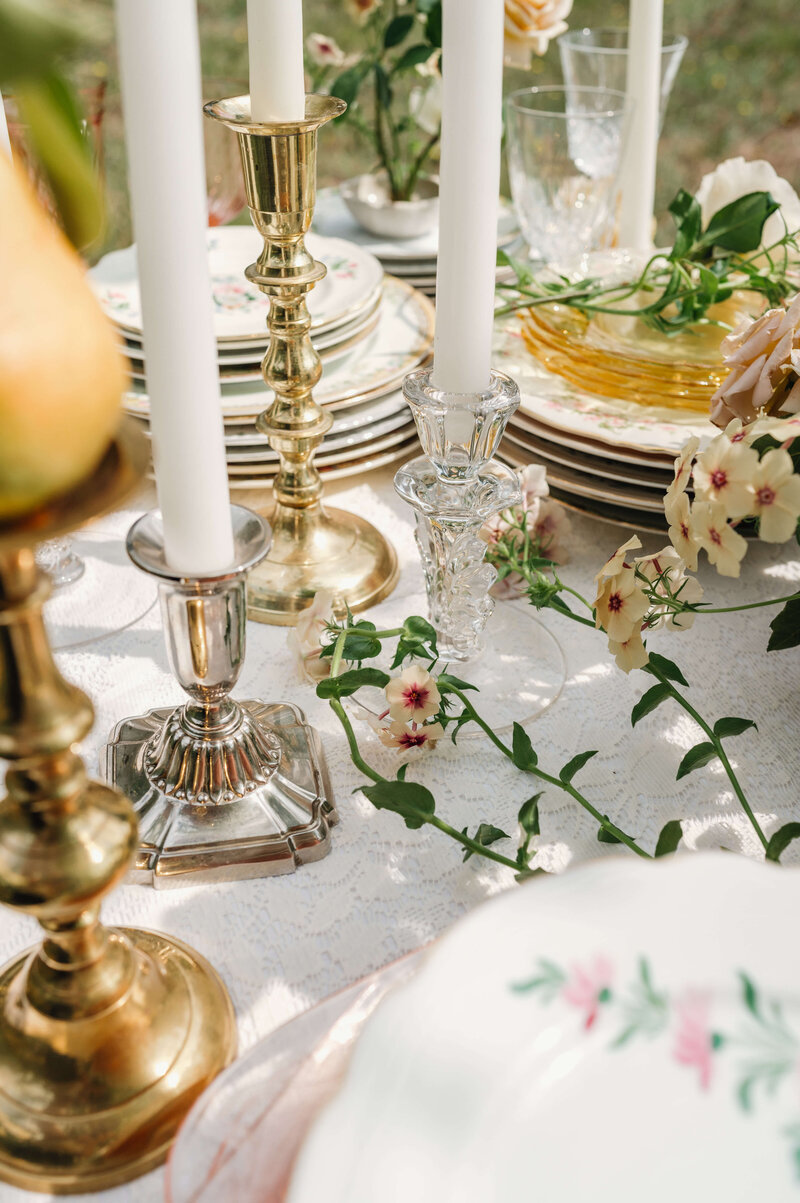 Candlesticks, plates and flowers on a table, representing event rentals by Birdie June. 