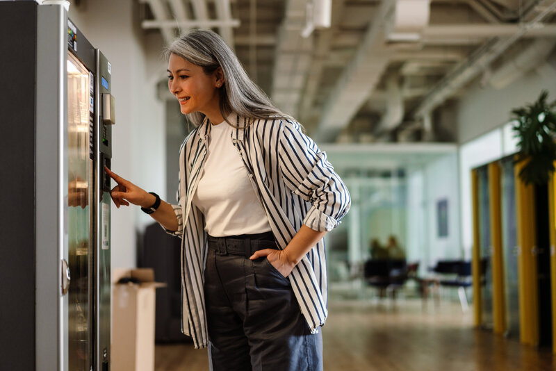 Smiling woman selecting an item from a vending machine in a modern workplace environment
