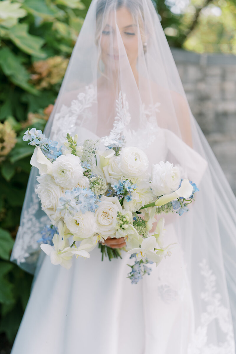 Bride with blusher veil holding blue, white, and cream colored wedding bouquet