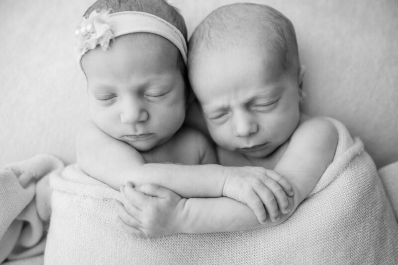 black and white image of newborn twins holding each other