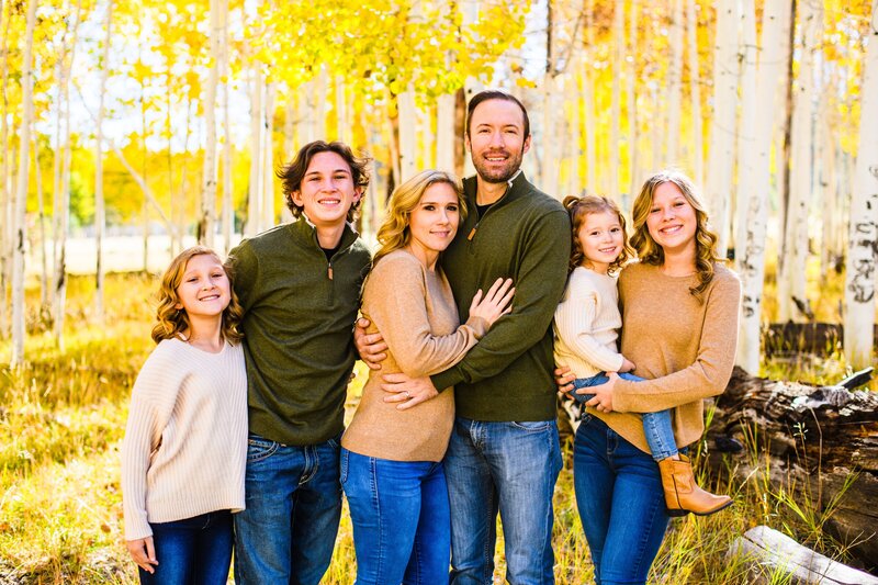 Large family in golden fall aspens in autumn in Flagstaff smiling and holding each other looking at camera