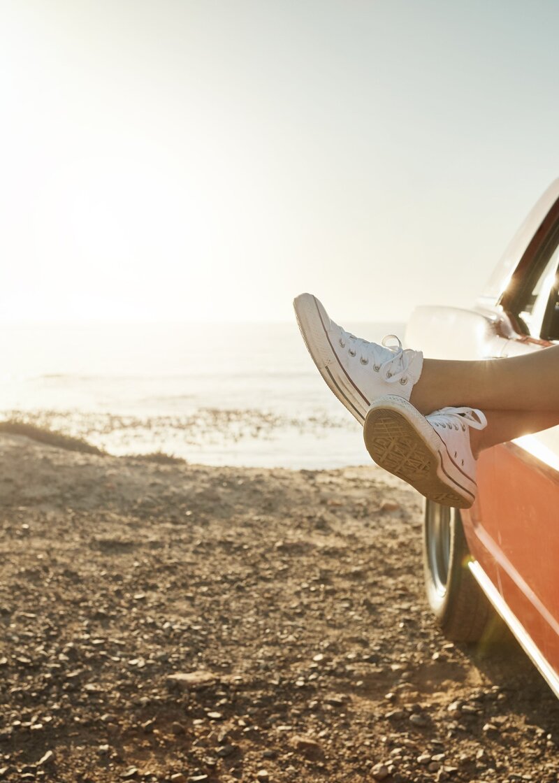 a pair of feet sticking out the window of a car on a beach while the sun shines wearing a pair of Converse shoes socialfizz