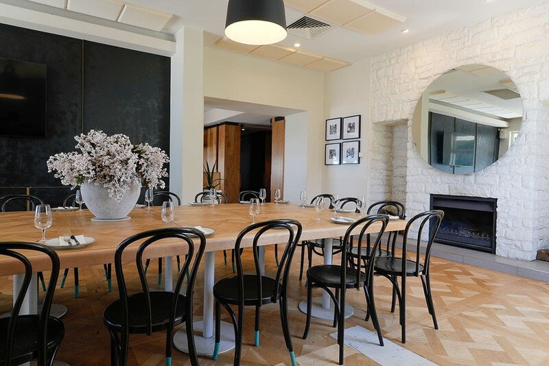 A wooden dining table with black chairs inside a restaurant with a large mirror on the wall.