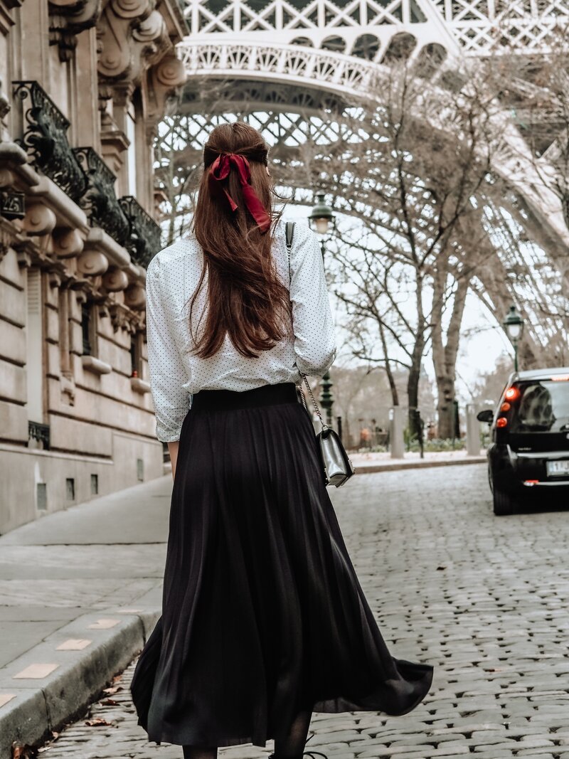 Woman in white blouse and black skirt standing looking at the Eiffel Tower in front of her in Paris France