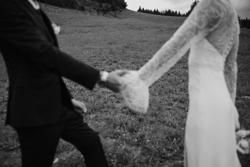 couple in black suit and white wedding dress lean close together while holding a white and green floral bouquet