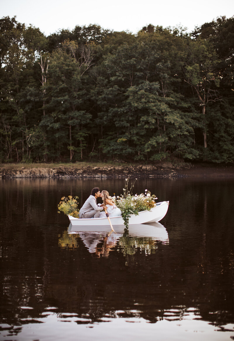 Bride and groom kissing in a flower-decorated rowboat on the water during their Maine elopement.
