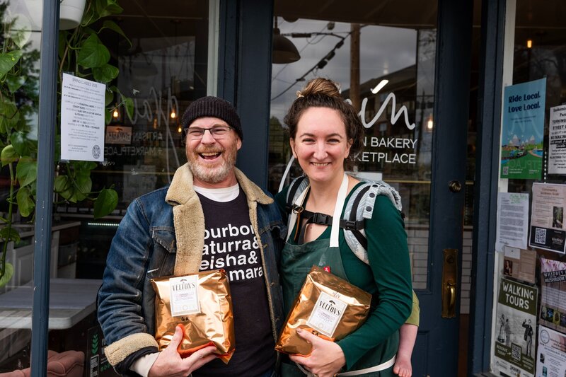 Grain Artisan Bakery founder standing with a local coffee roaster outside the Snohomish café, celebrating their Kickstarter-supported community partnerships and gluten-free mission.