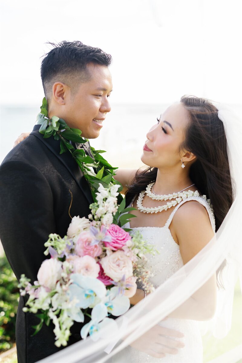 A wedding couple with their arms around each other smiling at each other 