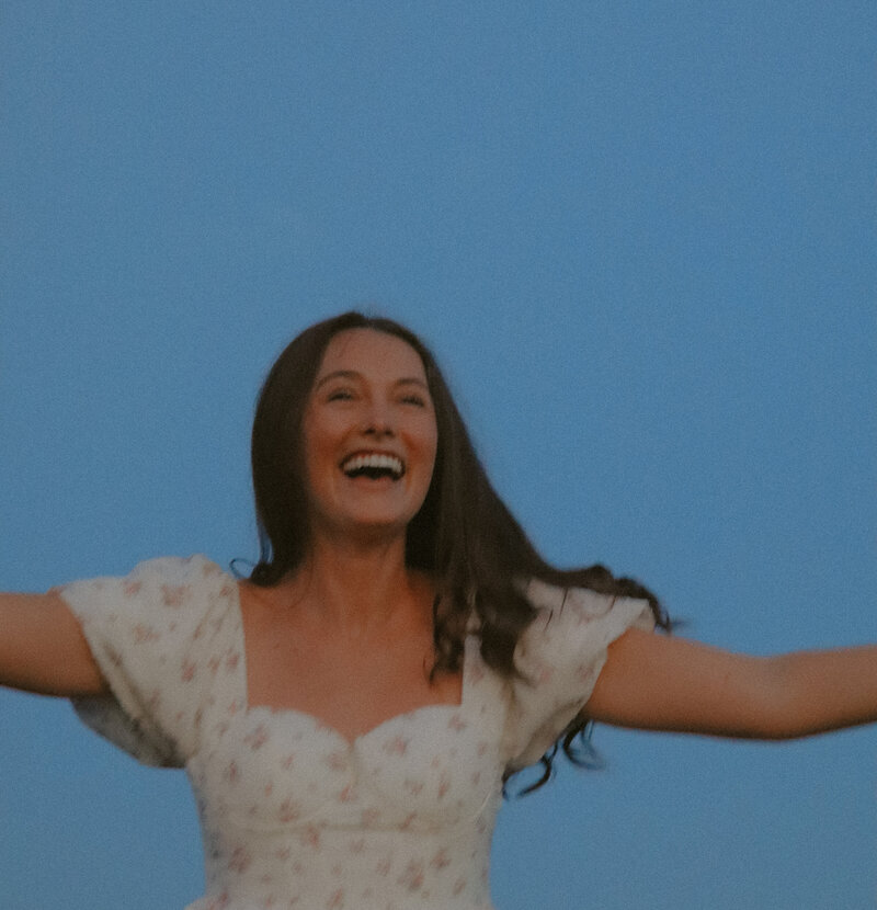 A woman has her arms in a T position while she has a big smile on her face.