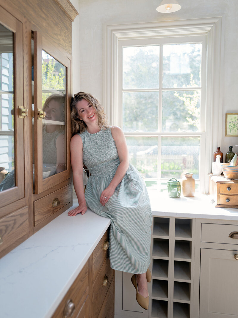 Headshot of Lauren Baker sitting on a marble kitchen counter in a maxi green dress and tan shoes