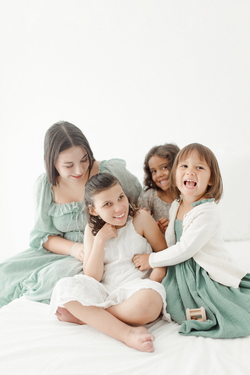 A family of four girls sitting on a bed tickling and laughing at each other during their family photography session in Panama City.