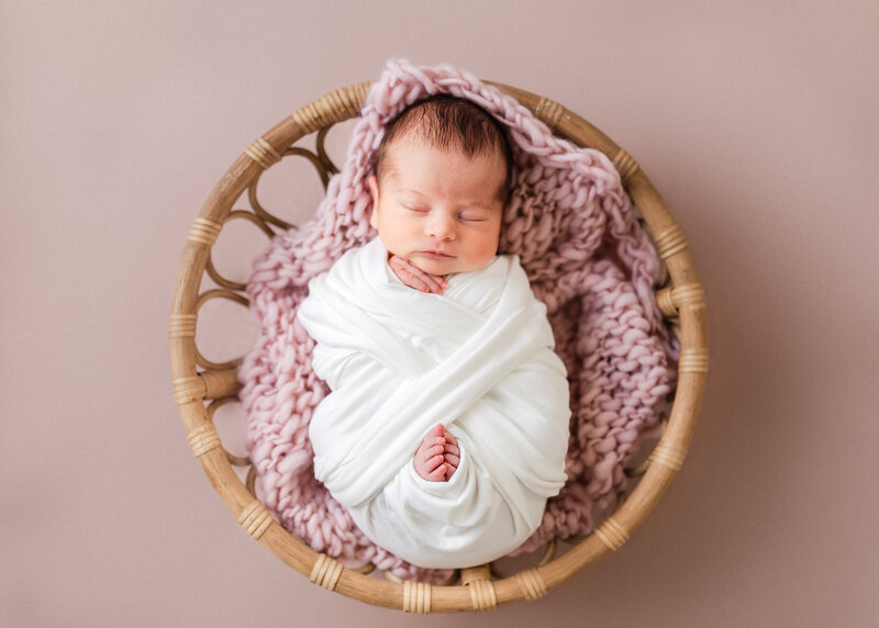 Posed and wrapped newborn in a boho basket at Allison Reilly's Union County, NJ photo studio.