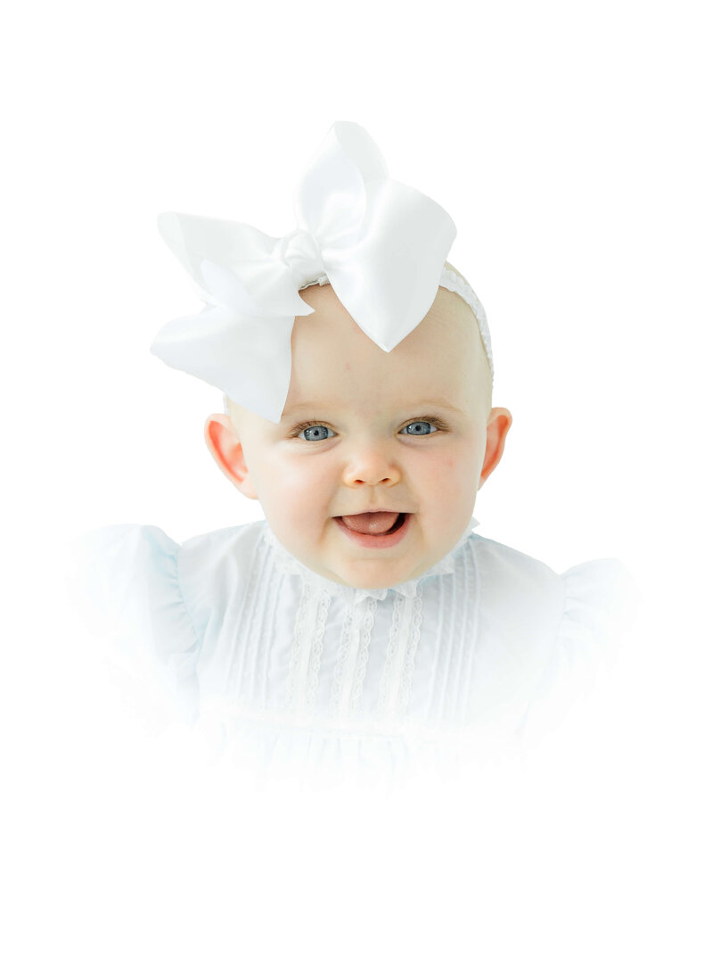Baby with a bow in an heirloom outfit posing for heirloom photography session in a Dothan Alabama Photography Studio