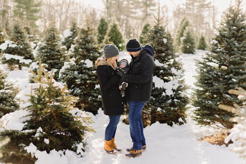 new parents posing for a photo during babies first christmas tree cutting by carrie pellerin