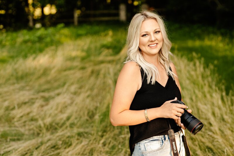 Melissa Lucci, a Pittsburgh, PA photographer in a black t-shirt and ripped jeans sitting on the floor smiling.