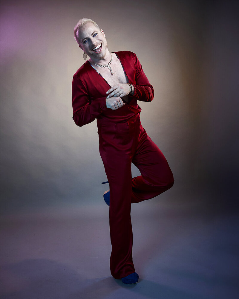 Full-body fashion portrait of Dain August in a red outfit, leaning gracefully in a studio setting with artistic lighting, captured by Ylva Erevall.